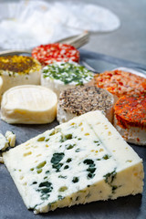 Assortment of French fresh white soft goat cheeses with different tastes topping made with herbs, paprika, indian curry, bruscetta, chives and dried tomatoes and piece of blue cheese Roquefort