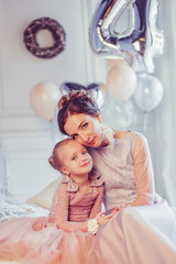 Fototapeta premium Close up portrait of elegant stylish mother and daughter in fashion dresses playing together, celebrating happy birthday. Baloons background, party concept. Childhoood, cute kid, carefull mother