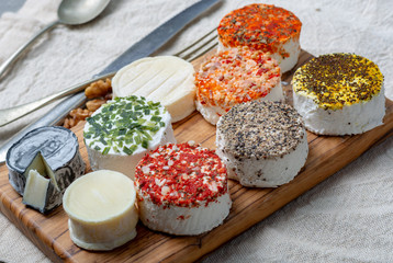 Assortment of French fresh white soft goat cheeses with different tastes topping made with herbs, paprika, indian curry, bruscetta, chives and dried tomatoes
