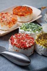 Assortment of French fresh white soft goat cheeses with different tastes topping made with herbs, paprika, indian curry, bruscetta, chives and dried tomatoes