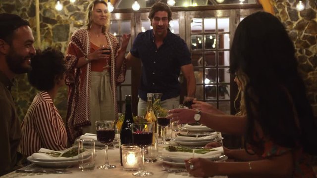 Host couple toasting drinks with guest at dinner party. Young people celebrating with drinks at party.