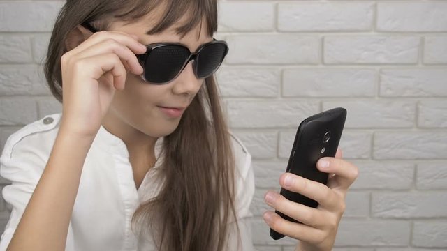 Teenage girl using smartphone and wearing pinhole glasses. Girl in glasses for training eyes look at the smartphone screen.