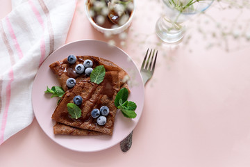 Homemade chocolate crepes served with blueberries, sauce and mint leaves on pink background. Selective focus. Top view. Copy space