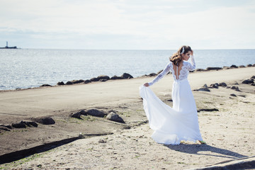 Fototapeta na wymiar Fashionable bride in elegant wedding dress walking on the coast of ocean. Beauty, emotional, lifestyle concept