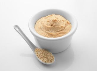 Bowl of tasty tahini with sesame seeds on white background