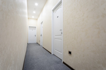 Lighted corridor milky color with three white doors and a white ceiling. Decorated in light...