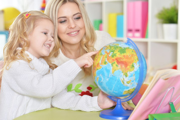 Portrait of mother with little daughter examine globe