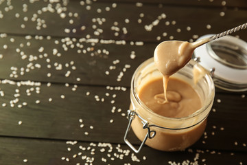 Spoon and jar with tasty tahini on wooden table
