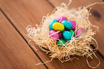 easter, confectionery and holidays concept - chocolate eggs in straw nest on wooden table