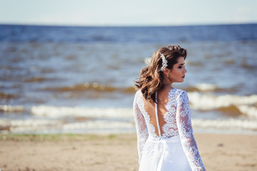 Fashionable bride in elegant wedding dress walking on the coast of ocean. Beauty, emotional, lifestyle concept