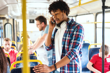 Young African American guy using smart phone for call while riding in the city bus. In background...