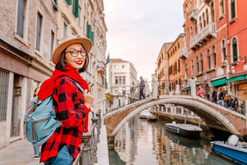 Fototapeta na wymiar Young happy asian traveler woman on the pier of a narrow canal and street in Venice. Vacation in Italy concept