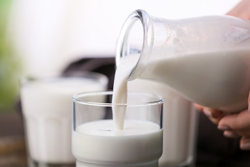 Pouring of fresh milk from bottle into glass, closeup