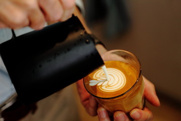 Barista using pitcher for pouring frothed milk to cup of coffee latte with tulip pattern on top