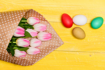Easter vibes. Spring holiday. Happy easter season. Collecting easter eggs. Colorful eggs and bouquet fresh tulip flowers on yellow background top view. Tradition celebrate easter. Sincere greetings