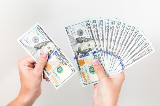 Closeup up view of white female hands holding many 100 dollars paper bills isolated on white background. Horizontal color photography.
