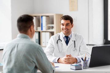 medicine, healthcare and people concept - smiling doctor talking to male patient at medical office...