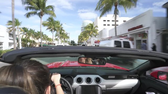 Backseat view of woman driving red convertible car in sunny Miami beach