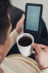 selective focus of cup with drink in hand of man reading ebook