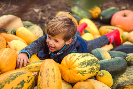 The smiling little boy lying on the pumpkins outdoors
