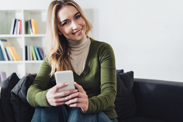 cheerful woman holding smartphone while sitting on sofa