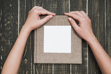 Closeup top view of female hands holding brown canvas photo book with empty white space in middle...