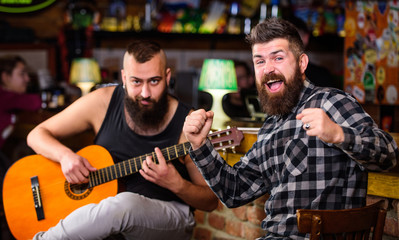 Man play guitar in pub. Cheerful friends sing song guitar music. Relaxation in pub. Friends relaxing in pub. Live music concert. Acoustic performance in pub. Hipster brutal bearded with friend in pub