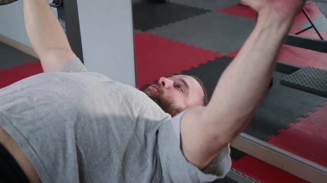 Handsome athletic man performs bench press on the bench in the gym.