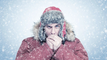 Fototapeta premium Frozen man in red winter clothes warming hands, cold, snow, frost, blizzard