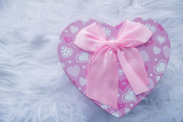 Pink box in the shape of a heart with a pink bow on a white fur rug.