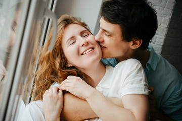 Happy girl and man kissing near window in home. 
