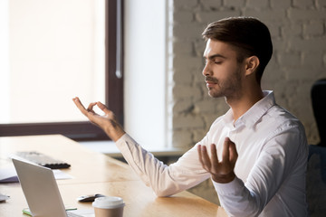 Peaceful worker meditating with eyes closed at office table