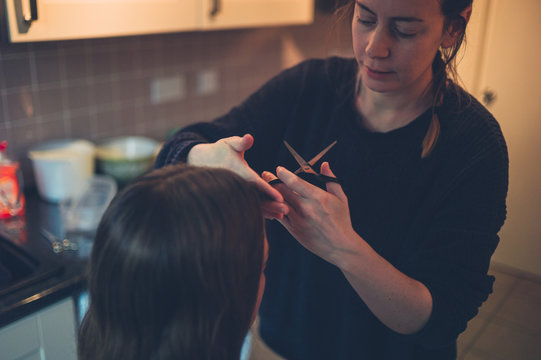 Woman cutting friend's hair in kitchen