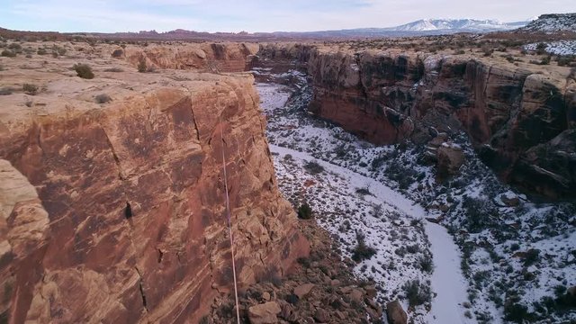 Flying over slackline on canyon rim down canyon in the Utah desert in winter near Moab.