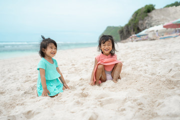 Fototapeta na wymiar two daughter sit down on white sand smiling at the camera