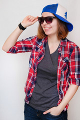 Naklejka premium Hipster in a plaid shirt, sunglasses and a cap. Young woman on white background.