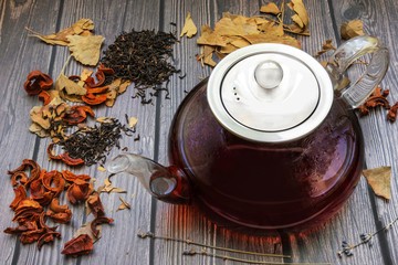 Teapot with tea, around a few kinds of tea on a dark wooden background