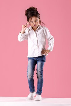 angry little child girl in white shirt with hairstyle looking to camera on pink background. Human emotions