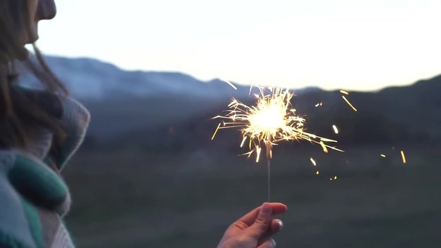 Female hand holds sparkler on a background of snowy mountains, beautiful sunset