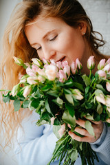 Portrait of a young beautiful girl with a bouquet of roses near window. Curly flowing red hair.
