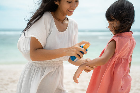 application sunblock to daughter skin before playing on the beach to protect from sun beath