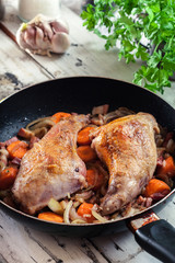 Fried rabbit legs on frying pan with vegetables