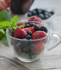 glass cup with berries, blueberries, raspberries, strawberries, and mint.On the wooden table light	