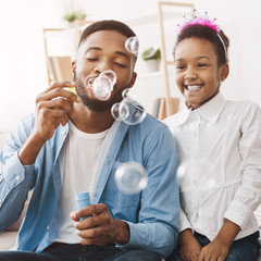 African-american family blowing soap bubbles at home
