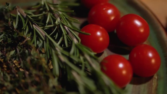 Fresh rosemary and tasty juicy red tomatoes lying on the kitchen board closeup. The camera moves from left to right.