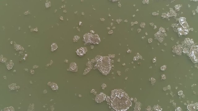 Rising aerial view above the Colorado river as ice floats down it in broken up chunks moving through the Utah desert.