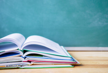 Stack of open books against the background of a green blackboard. School background