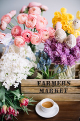 Beautiful spring flowers on the wooden table with easter decoration festive set: fresh blossoming ranunculus, Narcissus, hyacinths and tulips in the wooden box with espresso and cute toy chicken