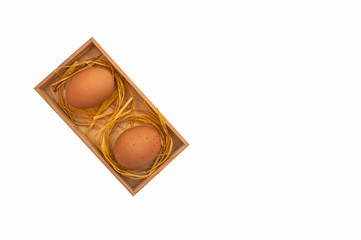 two brown chicken eggs in a box with straw in the nest top view