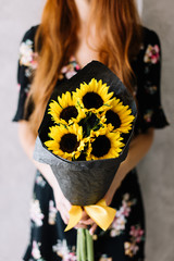Very nice young woman holding beautiful blossoming sunflowers mono bouquet on the grey wall...